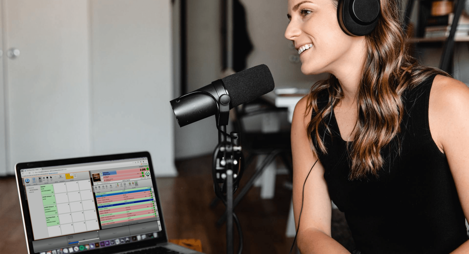 A woman wearing headphones is talking into a microphone in front of a laptop.