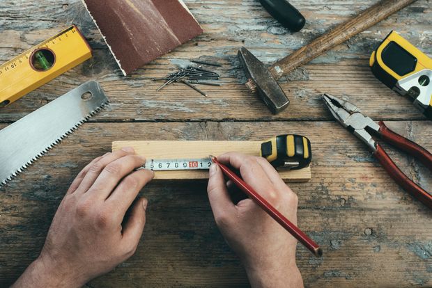 Mani che misurano una striscia di legno con una matita su un banco da lavoro con attrezzi
