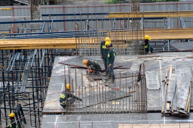 Operai edili su un pavimento di cemento accanto a barre d'armatura e impalcature in un cantiere.