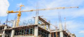 Cantiere edile con alte gru gialle sopra una struttura in acciaio parzialmente costruita sotto un cielo azzurro