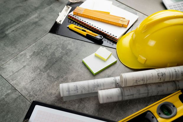 Progetti architettonici, elmetto giallo, righello, matita e metro a nastro su un tavolo da disegno.