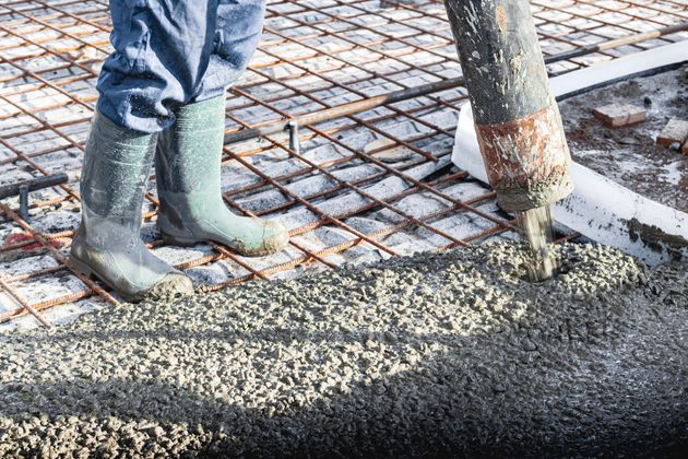 Un operaio versa cemento fresco accanto a degli stivali di gomma verdi in un cantiere.