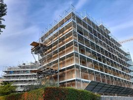 Le impalcature avvolgono un edificio a più piani in costruzione, stagliandosi contro un cielo azzurro.