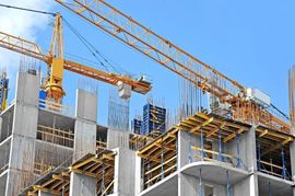 Cantiere edile con gru e una struttura in cemento parzialmente completata sotto un cielo azzurro e limpido.