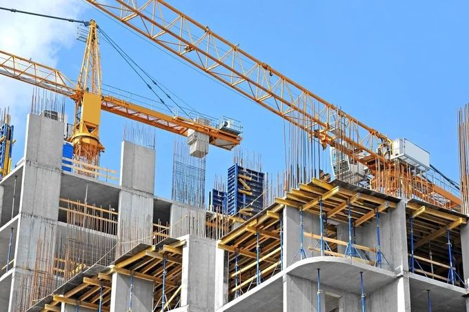 Cantiere edile con gru e una struttura in cemento parzialmente completata sotto un cielo azzurro e limpido.