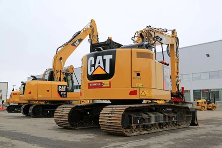 Un escavatore CAT giallo su cingoli è parcheggiato in un'area industriale, con un altro escavatore alle sue spalle.