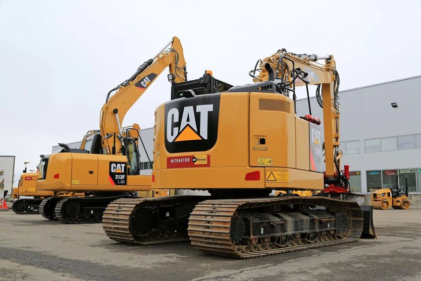 Un escavatore CAT giallo su cingoli è parcheggiato in un'area industriale, con un altro escavatore alle sue spalle.
