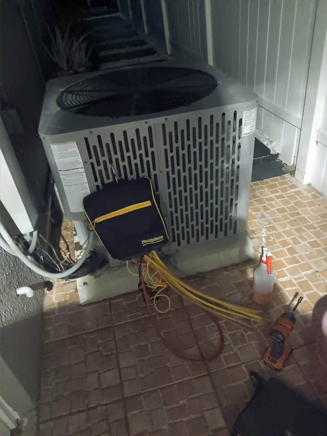 Outdoor air conditioner unit with maintenance tools and yellow service hose attached on a tiled patio