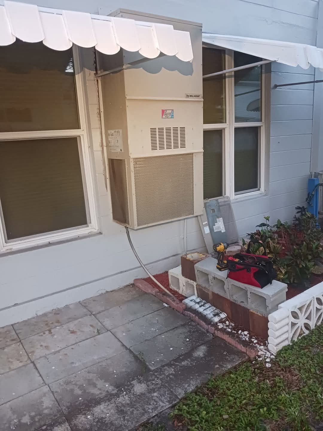 Small porch with awning, window AC unit, and white planter boxes beside a blue house