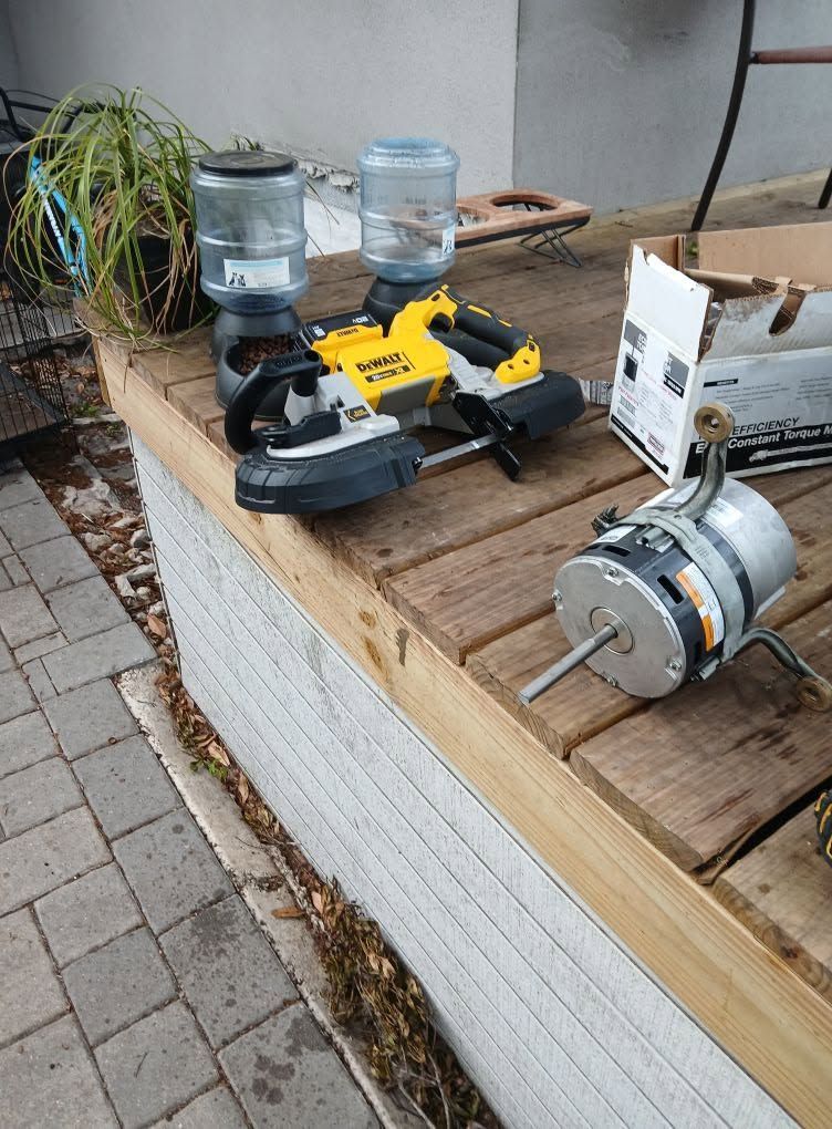 Workbench with a yellow-and-black miter saw, two glass jars, and a motor on a wooden table outdoors