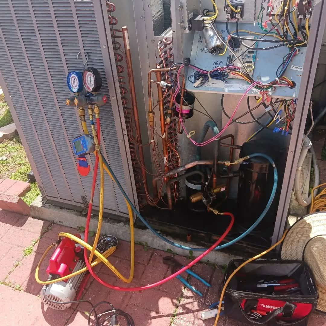 Open HVAC unit with manifold gauges, hoses, and tools on the ground during service