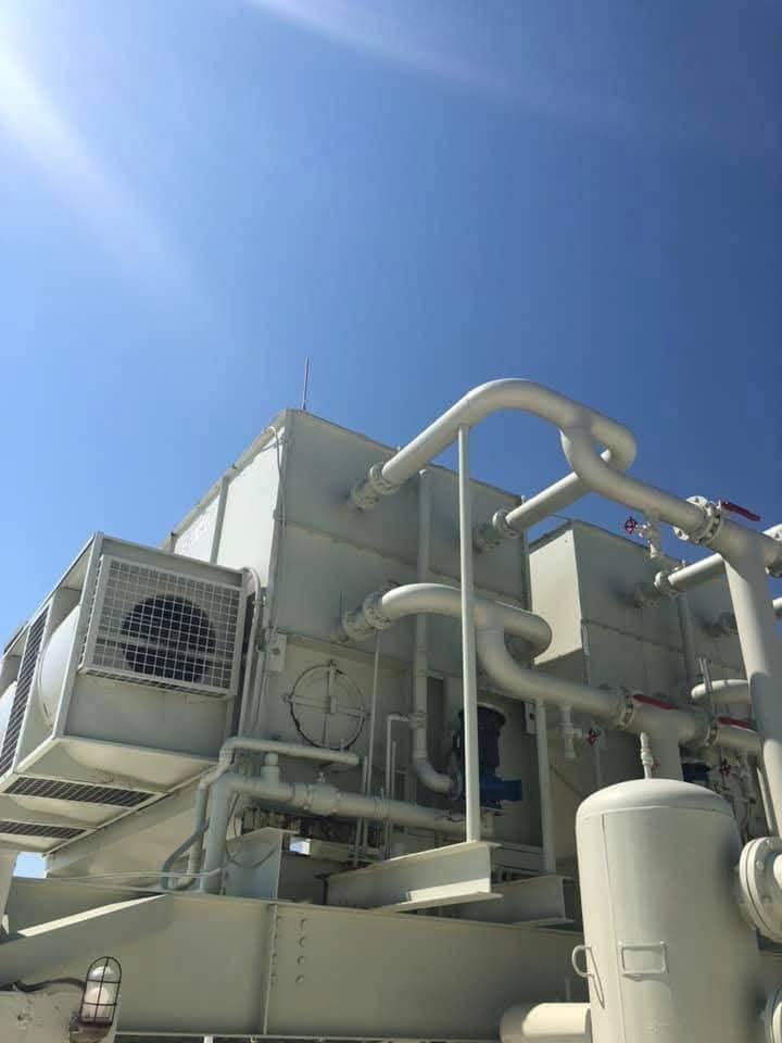 Industrial rooftop HVAC equipment with large white pipes under a bright blue sky