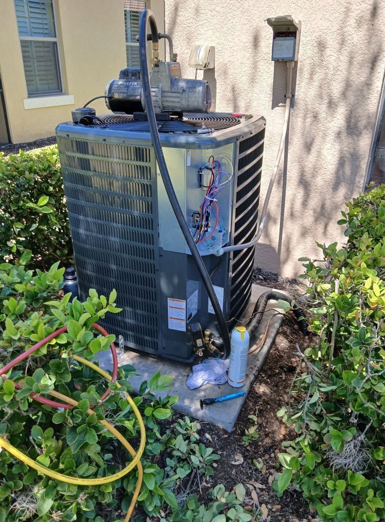 Outdoor air conditioner unit beside a house, with garden hose and tools around it