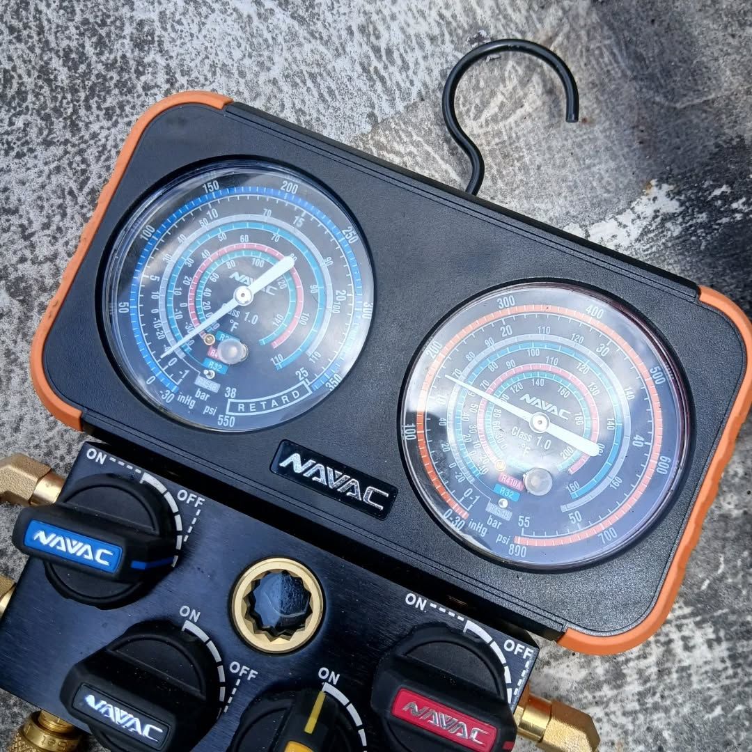 Portable car AC manifold gauge set with black case, blue/red dials, and hoses on a concrete surface
