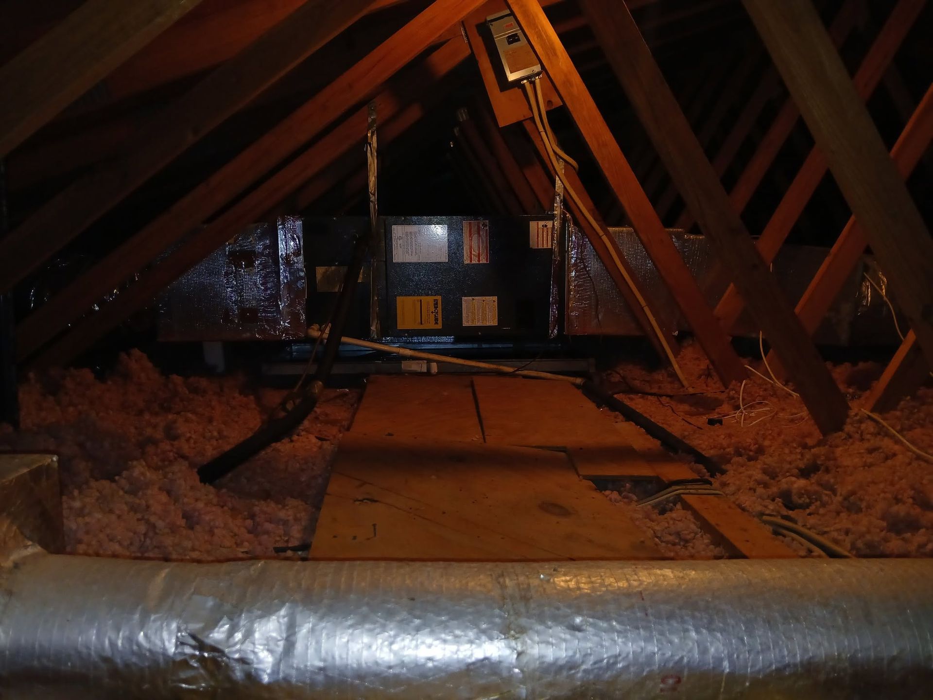 Attic interior with exposed wooden rafters, insulation, and a small lit window at the far end