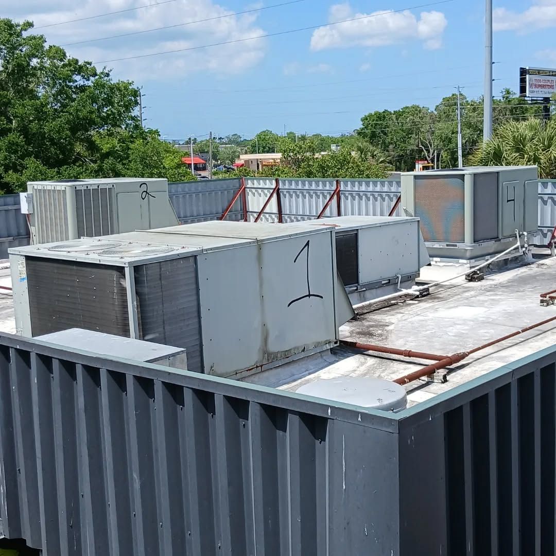 Rooftop HVAC units and ductwork on a flat roof with trees and sky in the background