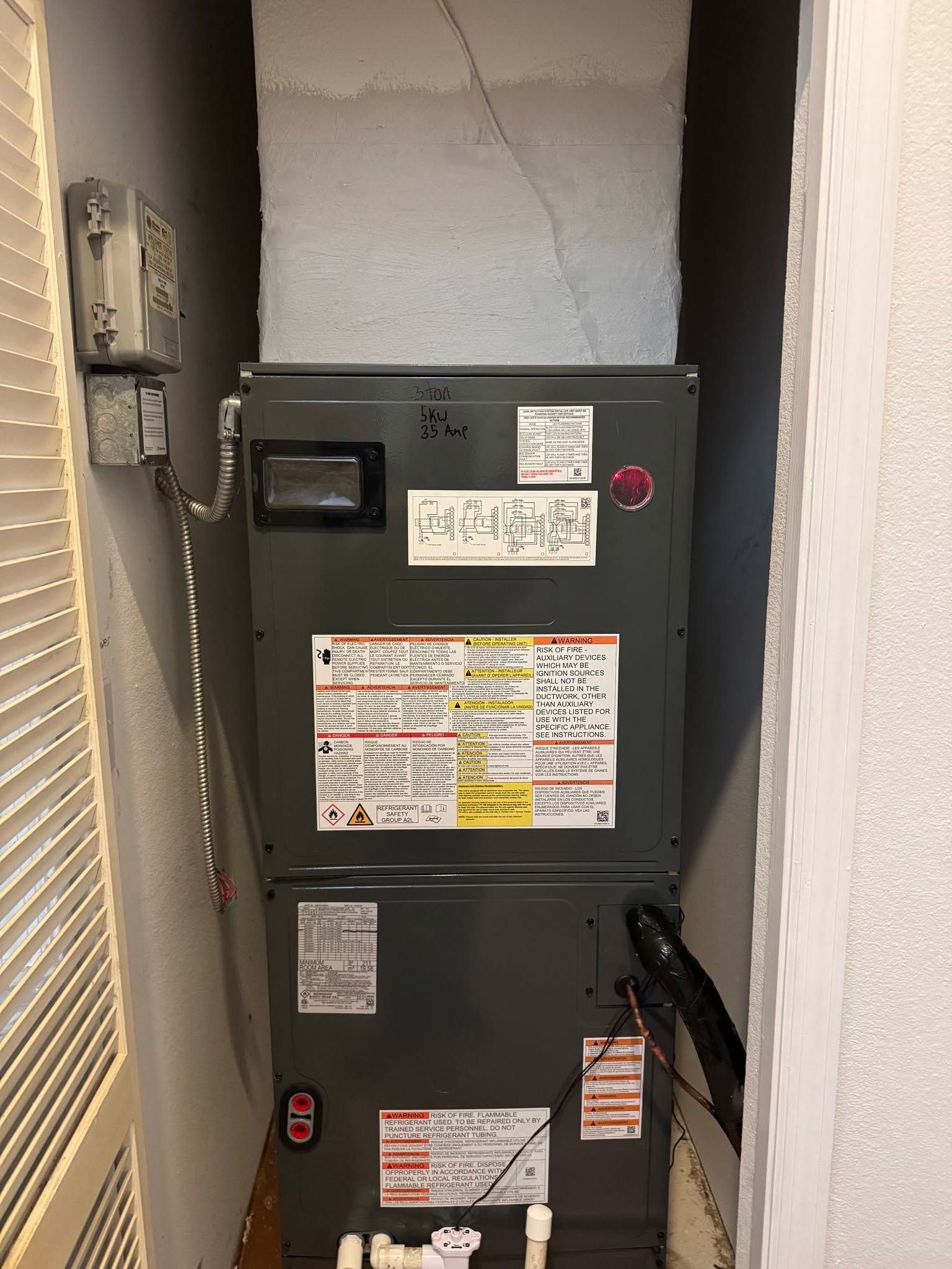 Gray electrical panel in a narrow hallway, with warning labels and exposed wiring along the wall.
