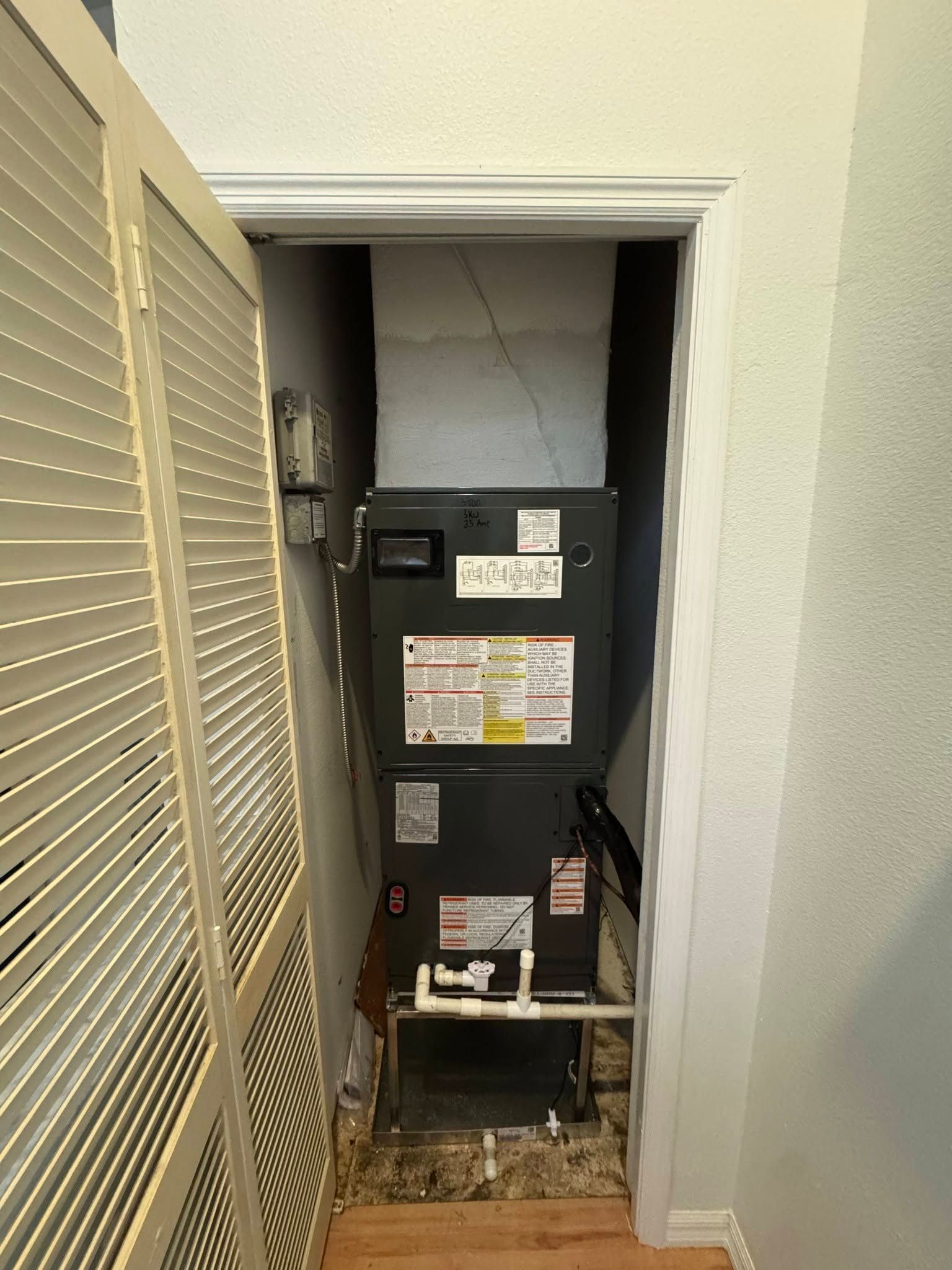Open closet with a furnace unit and exposed floor opening, viewed through a narrow doorway.