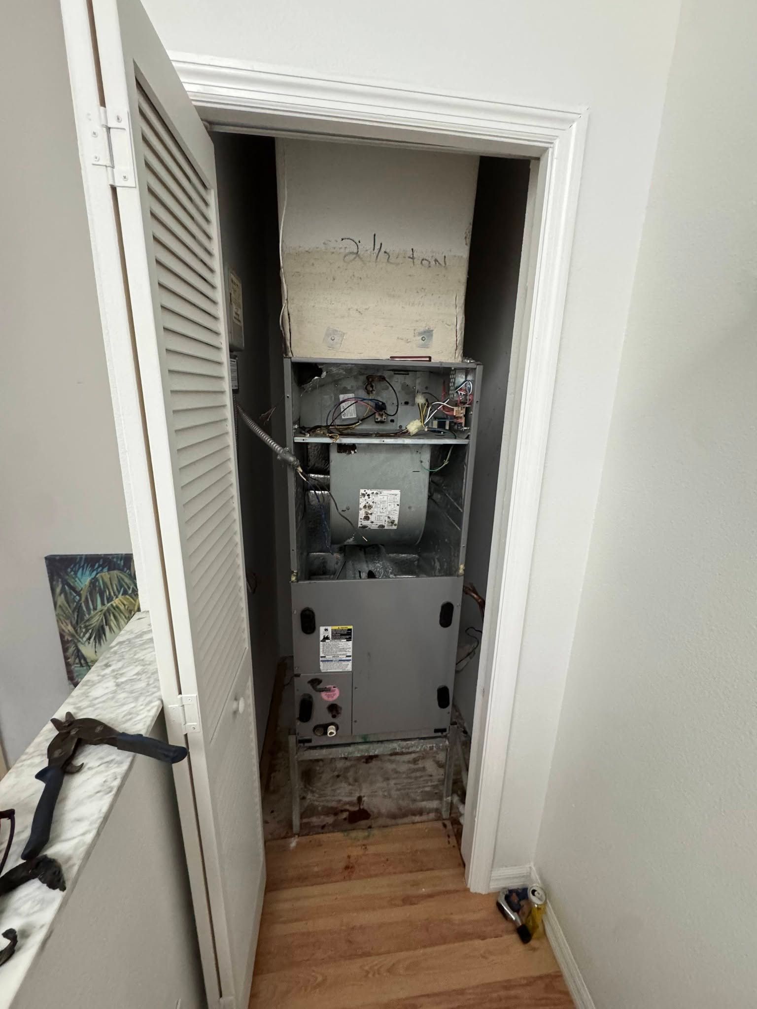 Open utility closet with exposed HVAC equipment and pipes above a wooden floor