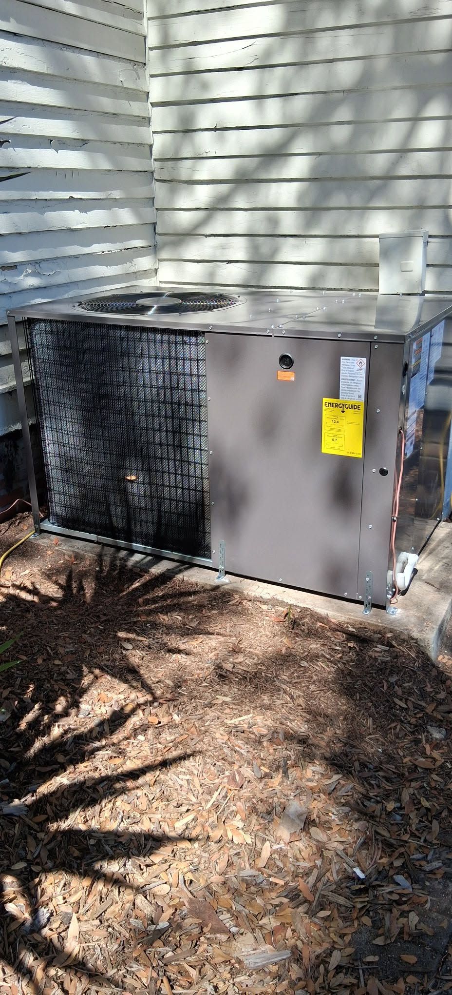 Outdoor air conditioning unit beside a house with white siding and mulch ground