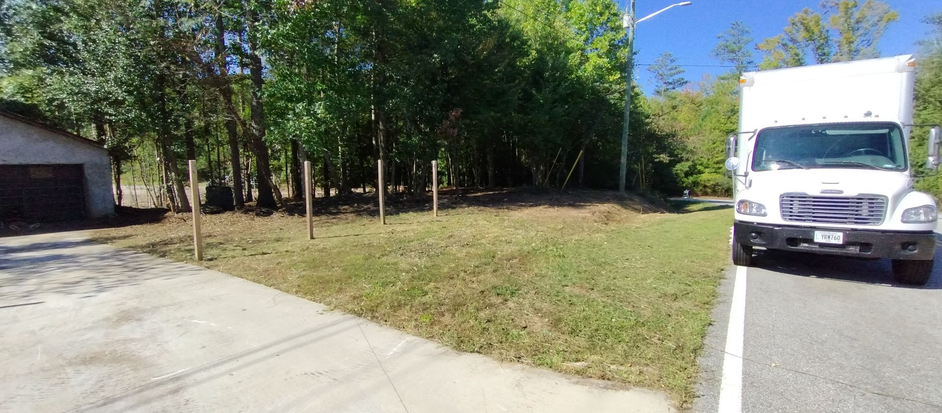 A white box truck parked on the side of a rural road next to a grassy lot with a concrete driveway and trees. A white box truck parked on the side of a rural road next to a grassy lot with a concrete driveway and trees.