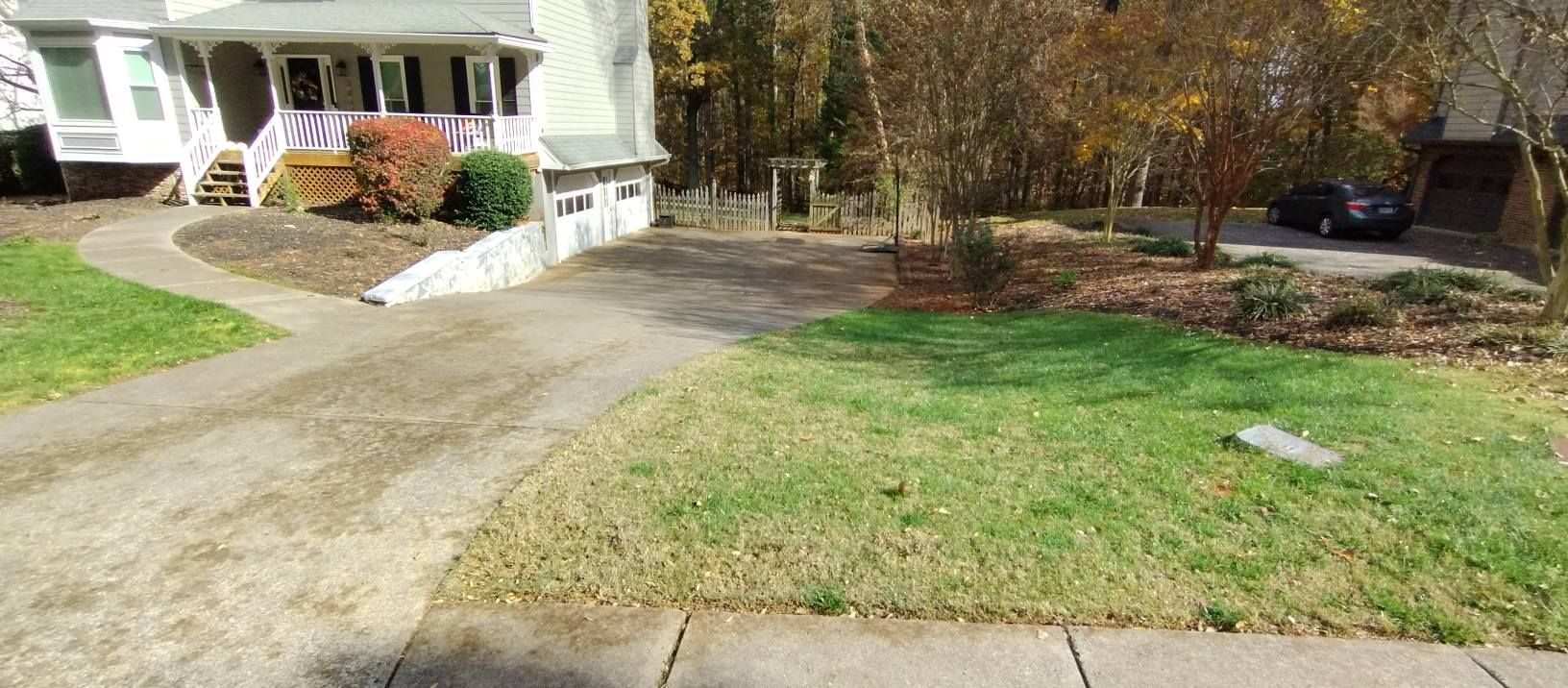 A paved driveway leads to a light-colored house with a small front yard and surrounding trees on a sunny day. A paved driveway leads to a light-colored house with a small front yard and surrounding trees on a sunny day.