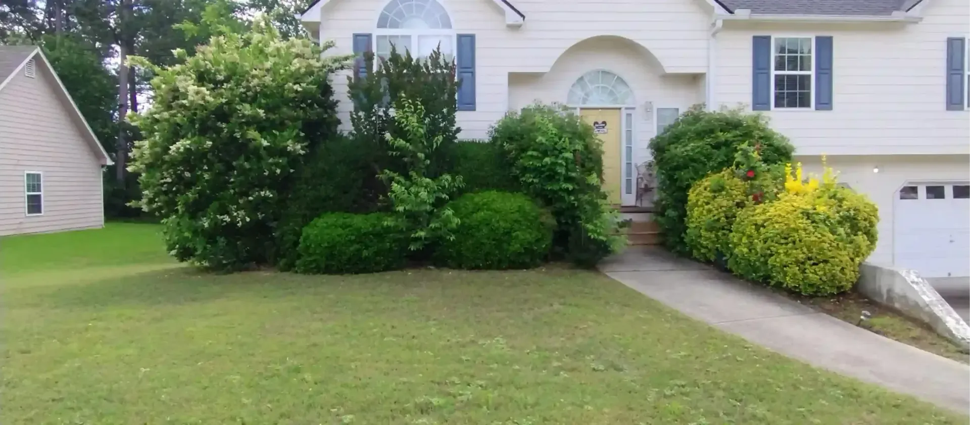 A white, two-story house with a yellow front door, blue shutters, and manicured landscaping in the front yard.