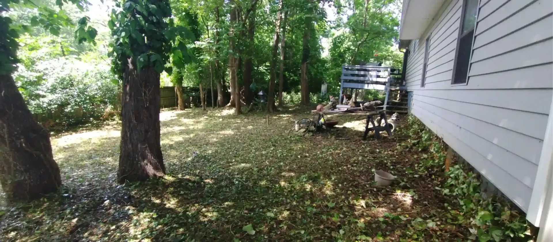 A side yard with light-colored siding, several large trees, and a wooden wagon wheel display against the house.