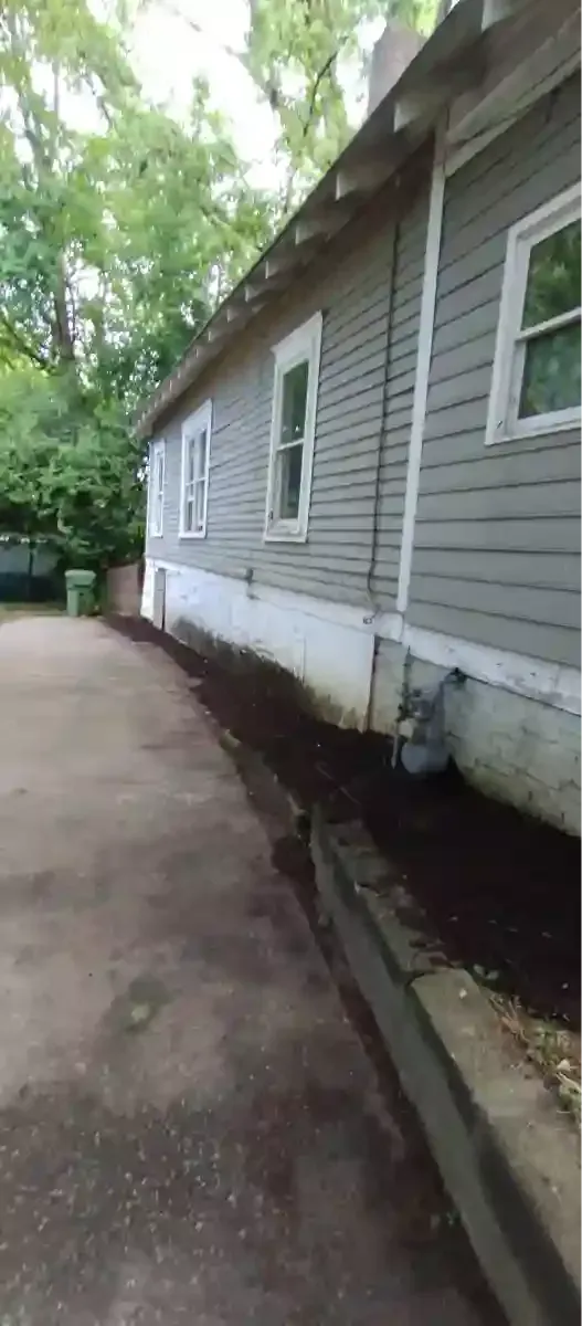 A gray house exterior with white trim and foundation, alongside a paved driveway with a newly mulched garden bed.