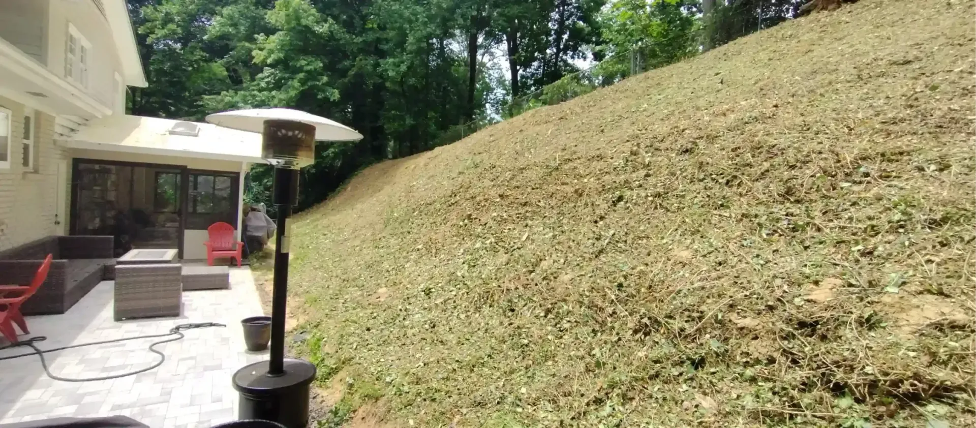 A view from a patio looking up at a steep, freshly mowed grassy hill next to a house.