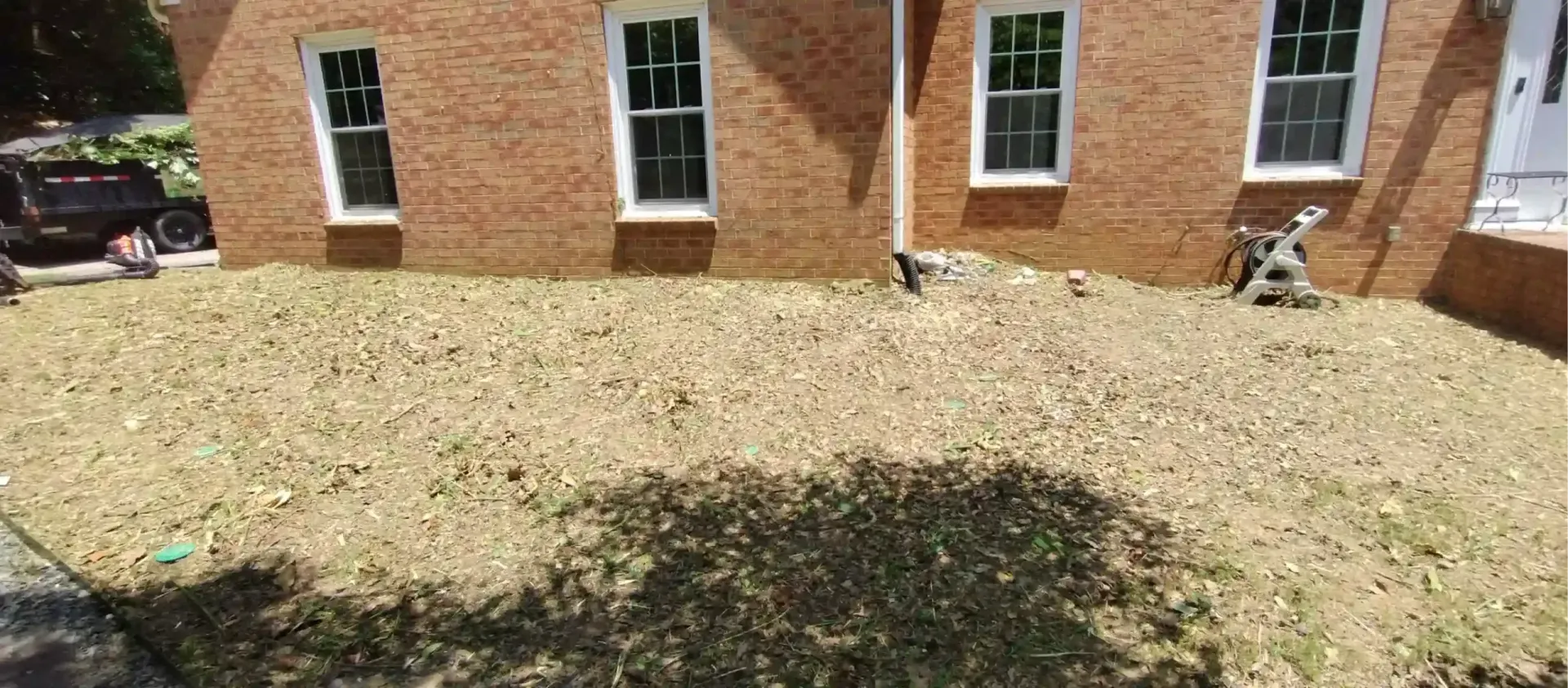 A brick building exterior with a lawn covered in scattered leaves and debris, with a black vehicle visible on the left.