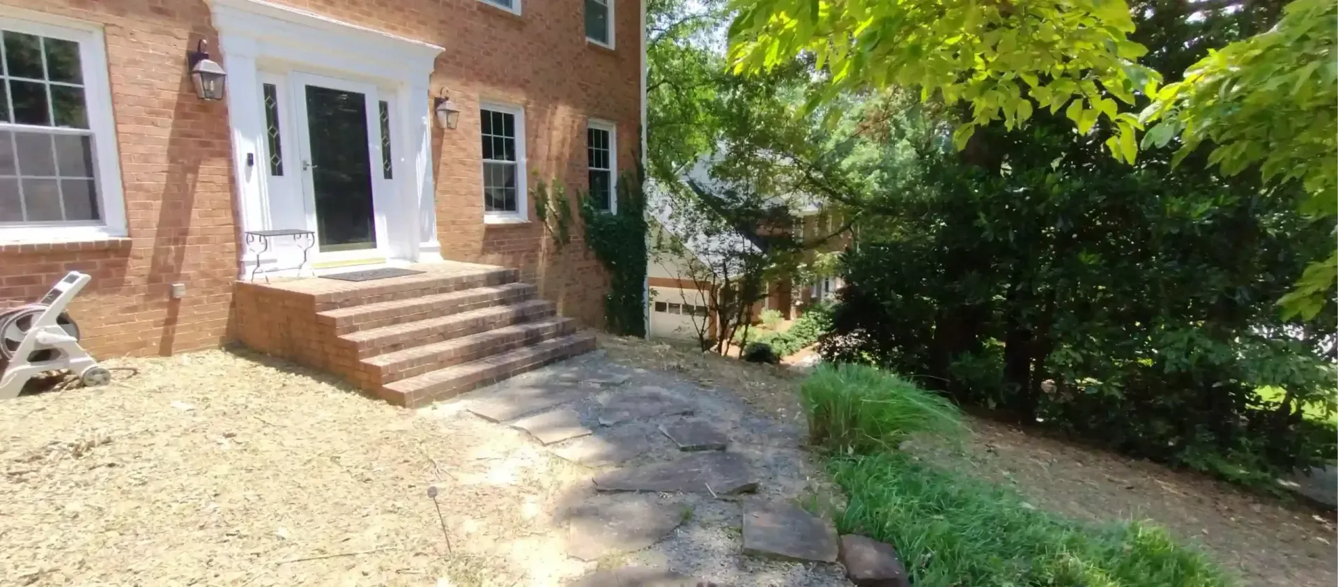 A brick house with a white front door and stone steps leading up to the entrance from a flagstone path.