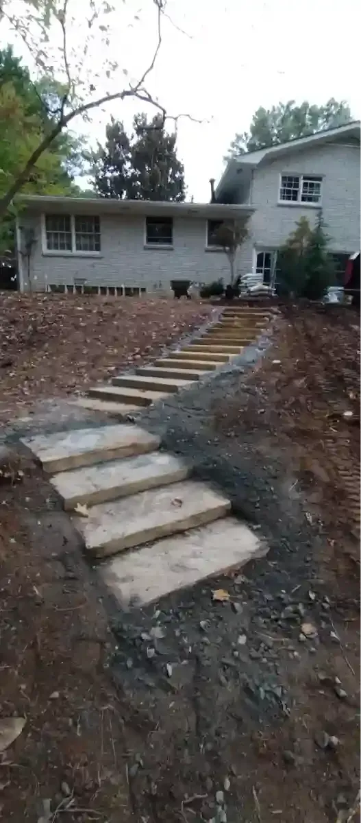 A set of wide, light-colored stone steps leading up a dirt hill toward a white suburban house.