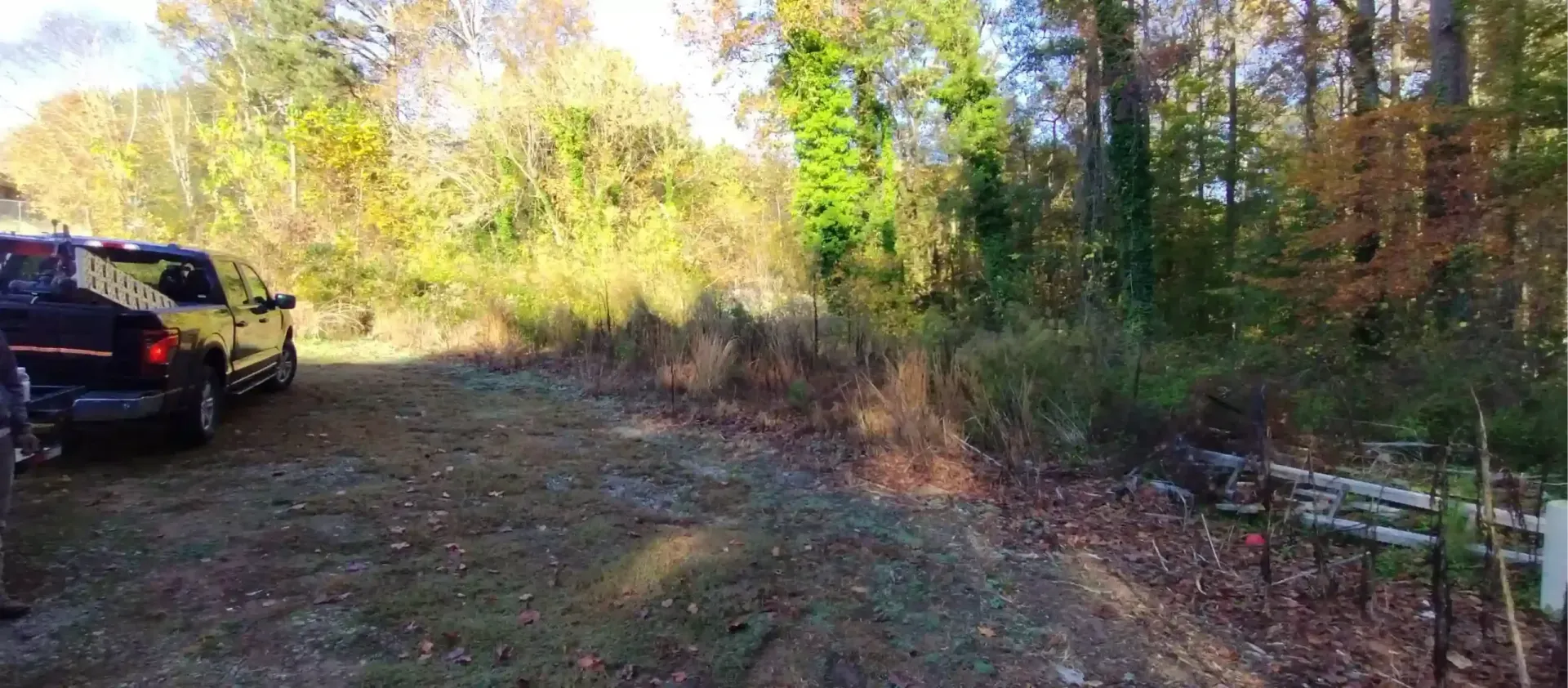 A black SUV parked on a gravel path at the edge of a forest with autumn foliage.