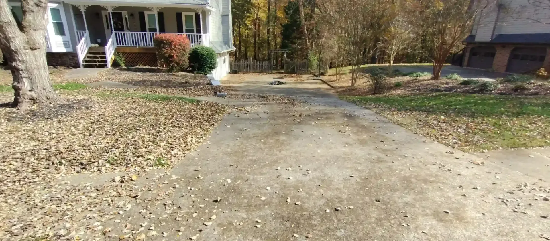 A driveway covered in fallen leaves leading to a house with a front porch, viewed on a sunny day.