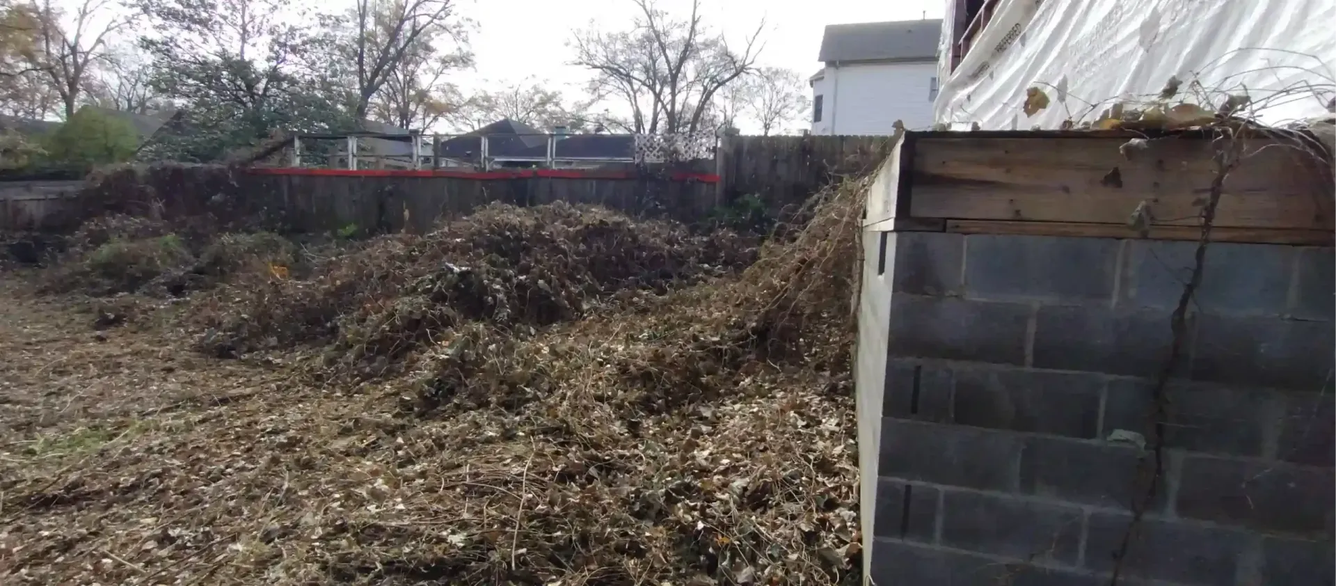 A large pile of wood chips sits near the gray concrete block foundation of a building under construction.