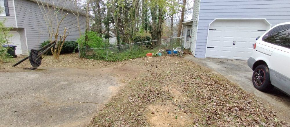 A grassy front yard between two houses with a driveway, a parked car on the right, and scattered leaves on the ground.