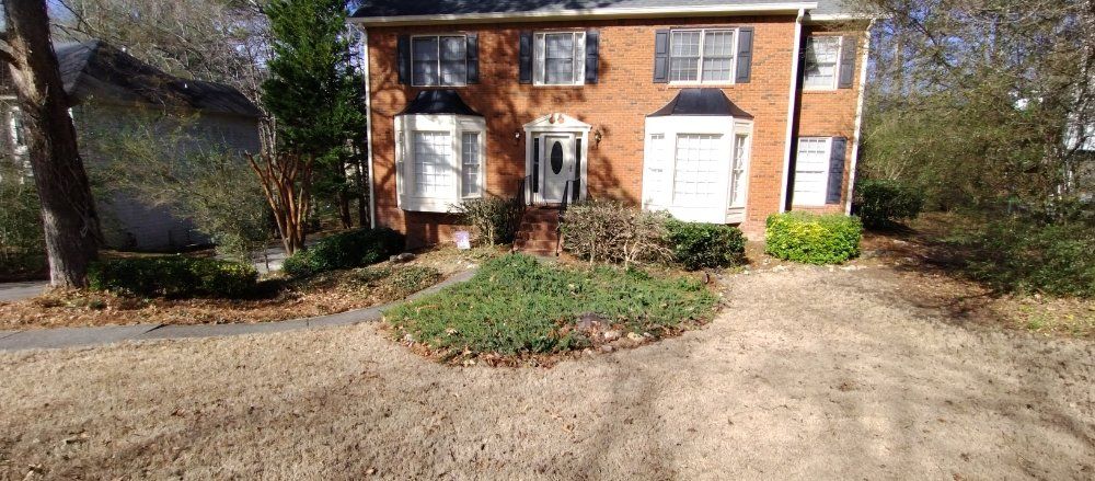 A two-story red brick house with white trim, a central front door, and a dormant lawn with landscaping in front.