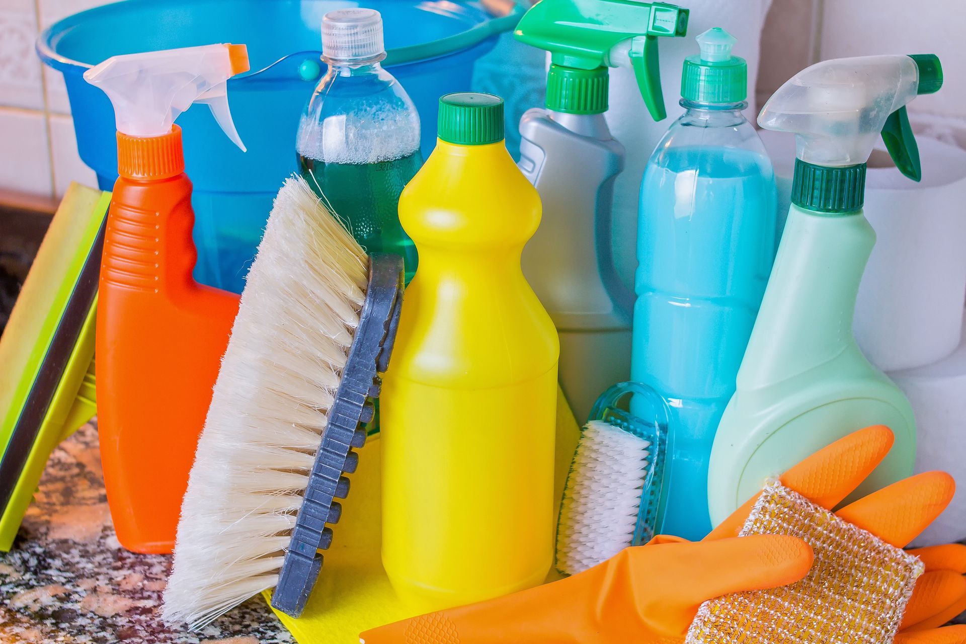 Varios botes de spray de limpieza de colores, cepillos y esponjas dispuestos sobre una encimera.