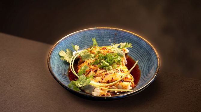 Blue bowl of pasta garnished with herbs and vegetables on a dark table