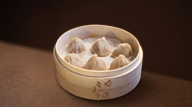 Steamed dumplings in a round bamboo basket on a dark table