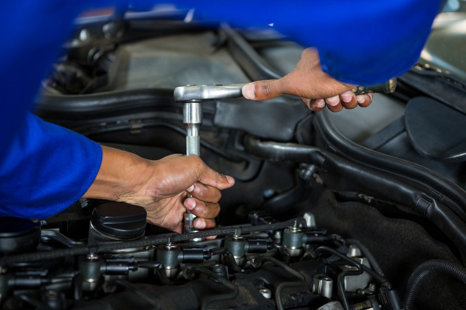 Mecánico utilizando una llave de carraca para reparar el motor de un coche bajo el capó.