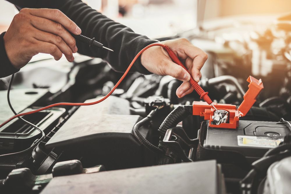 Manos usando cables de arranque para cargar la batería de un coche en el compartimento del motor.