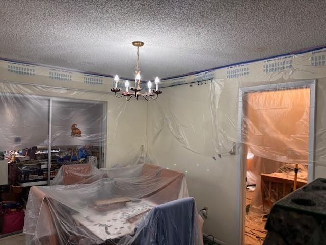 Living room under renovation, with furniture covered in plastic and an open doorway to a lit room.
