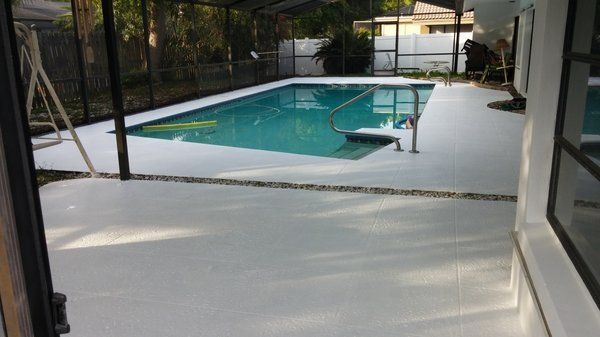 Patio view of a backyard swimming pool with turquoise water and a metal handrail, framed by a white deck and screened 