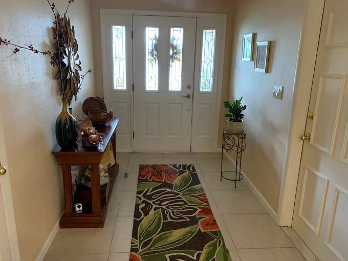 Bright entryway with white front door, floral runner rug, console table, and small plant stand