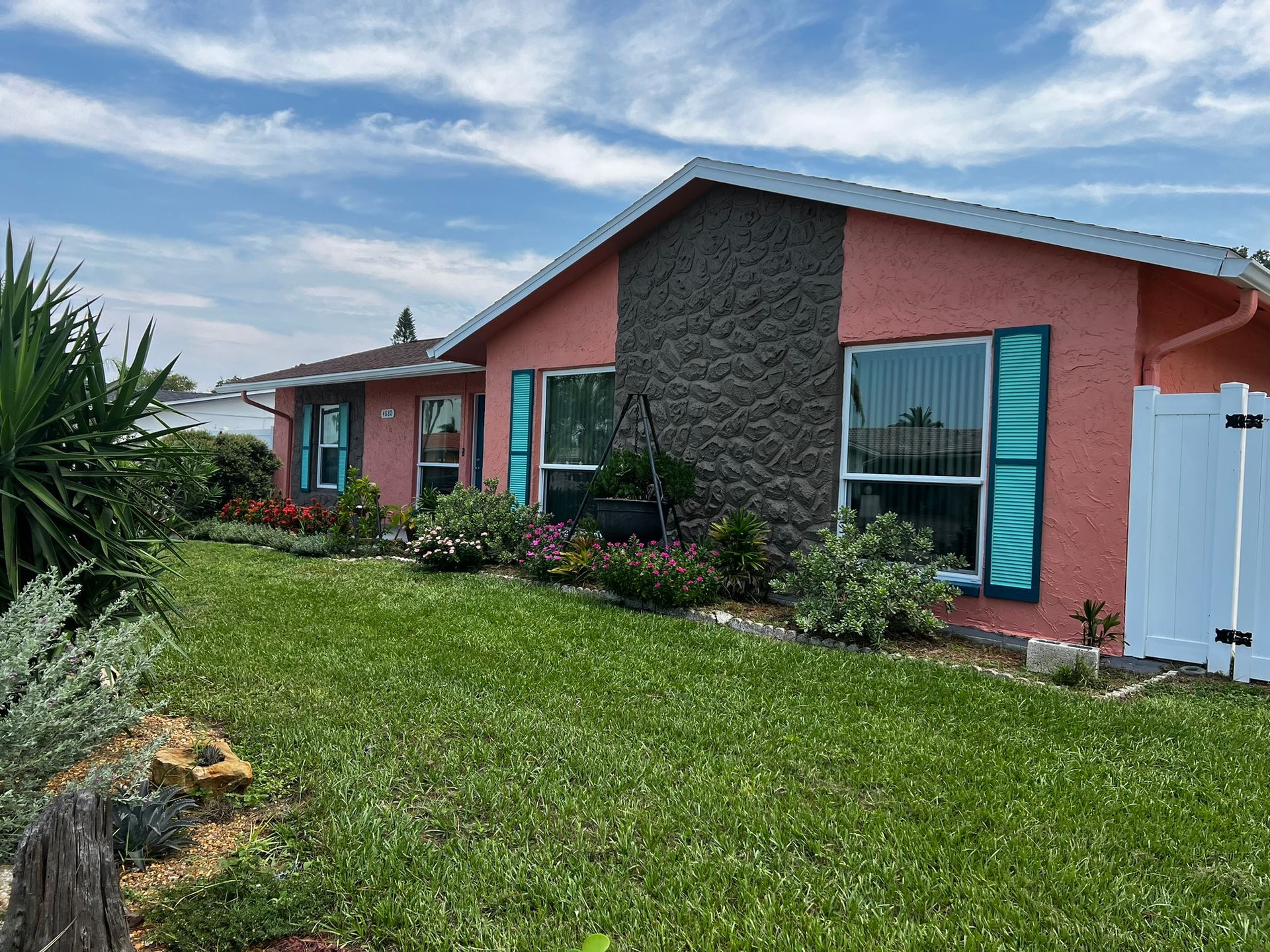 Single-story coral house with teal shutters, stone façade, and a green lawn under a blue sky.