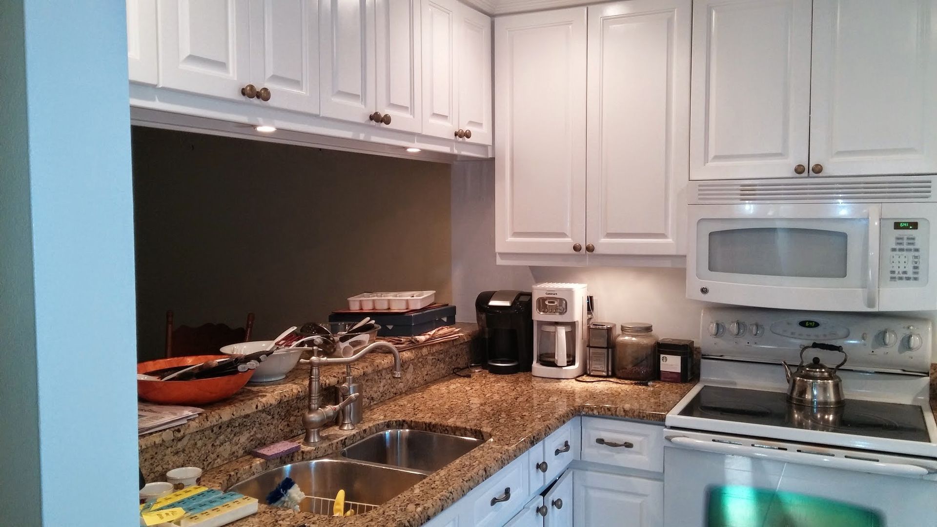 White kitchen with granite counters, sink, stove, microwave, and coffee maker; one cabinet door open.