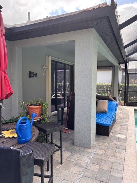 Patio seating area with a blue-cushioned bench, black table, potted plants, and a red umbrella beside a house