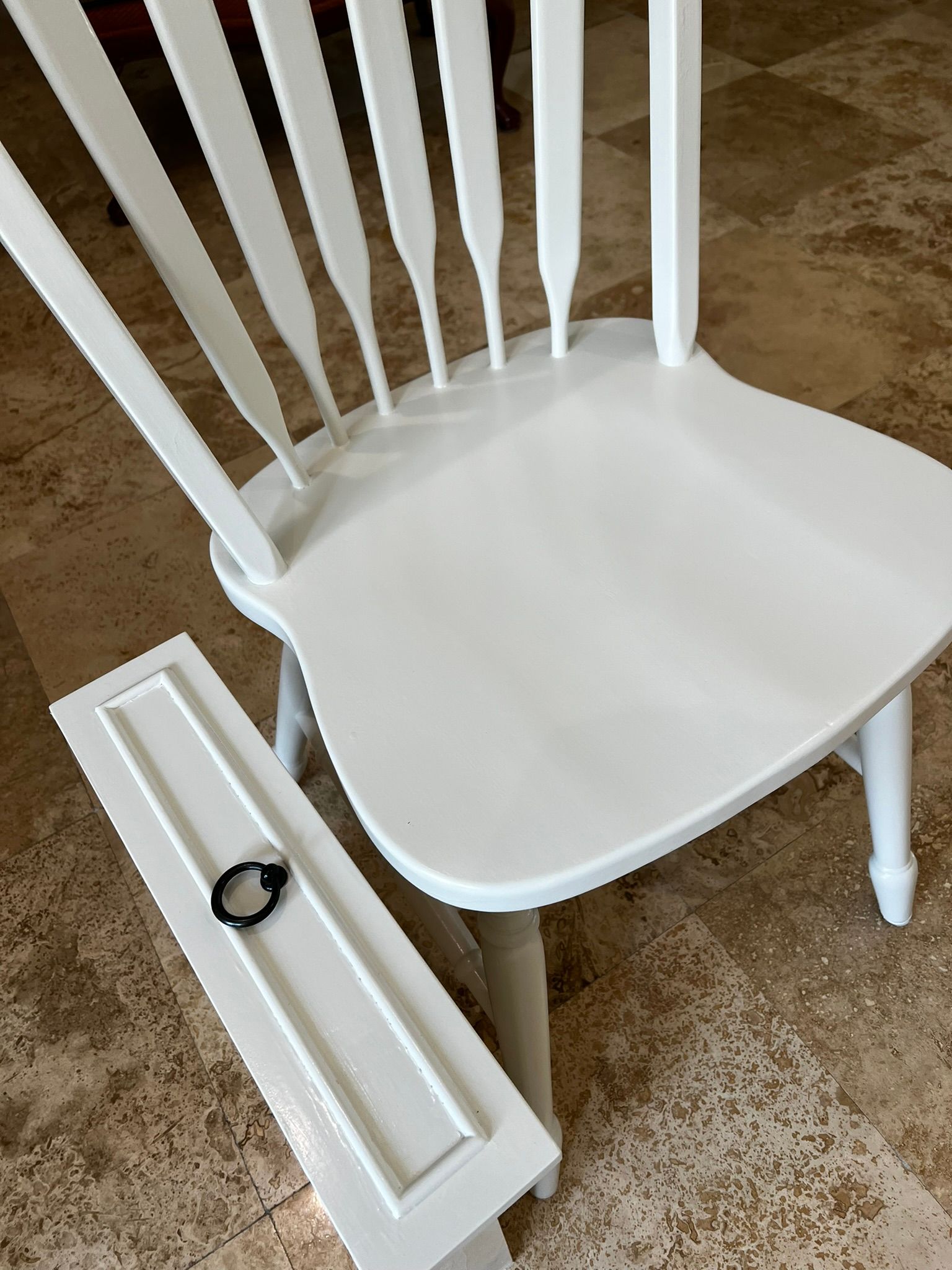 White wooden chair with a detached drawer-like piece leaning against it on a tan carpet.